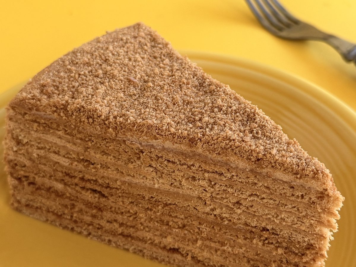 A honey cake cut open to show thin honey layers and cream, coated in crumbs
